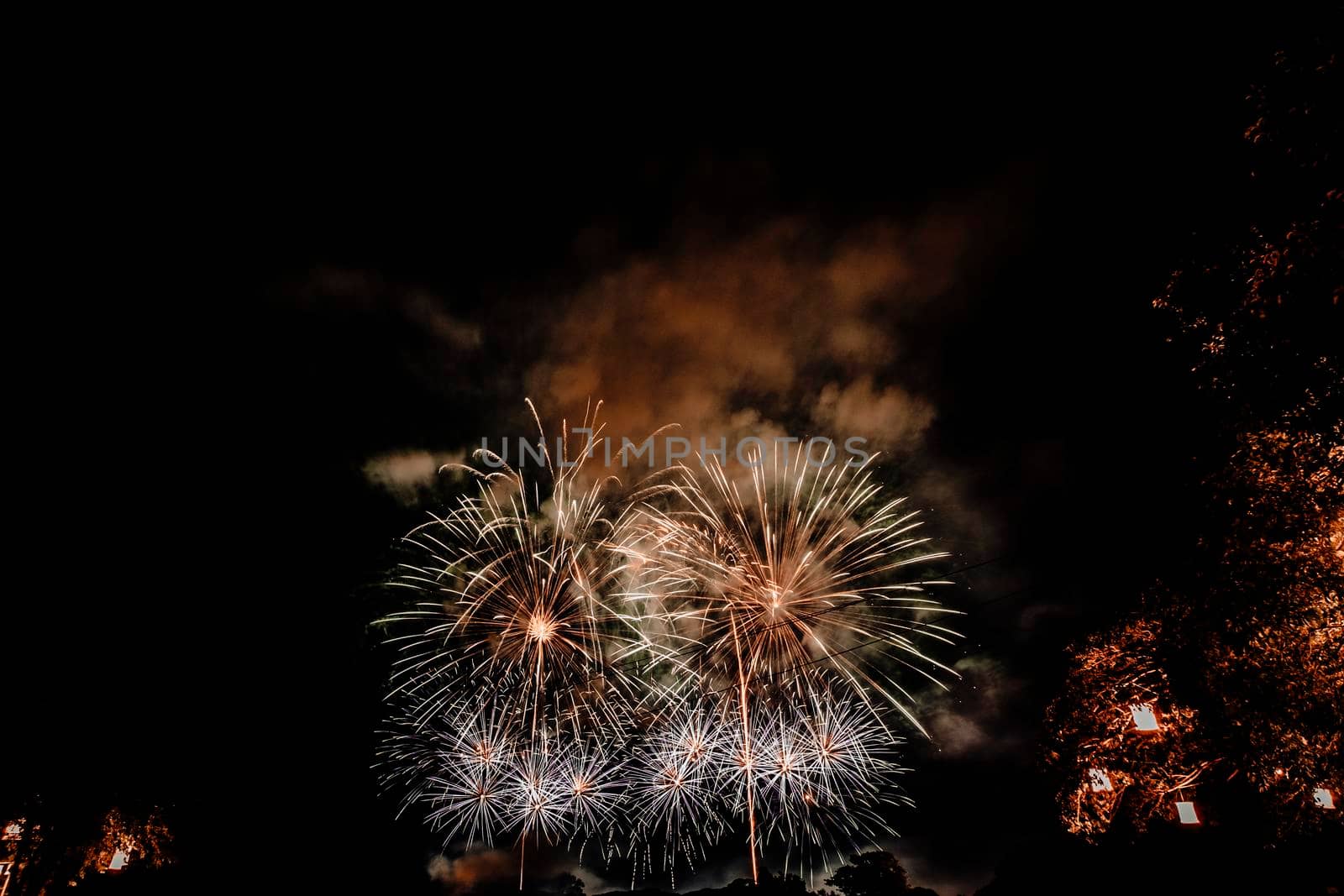 Group of people watching fireworks and using cellphones to record event. People capturing a fireworks shows with their mobile phone. Colorful fireworks celebration and the night sky background by Petrichor