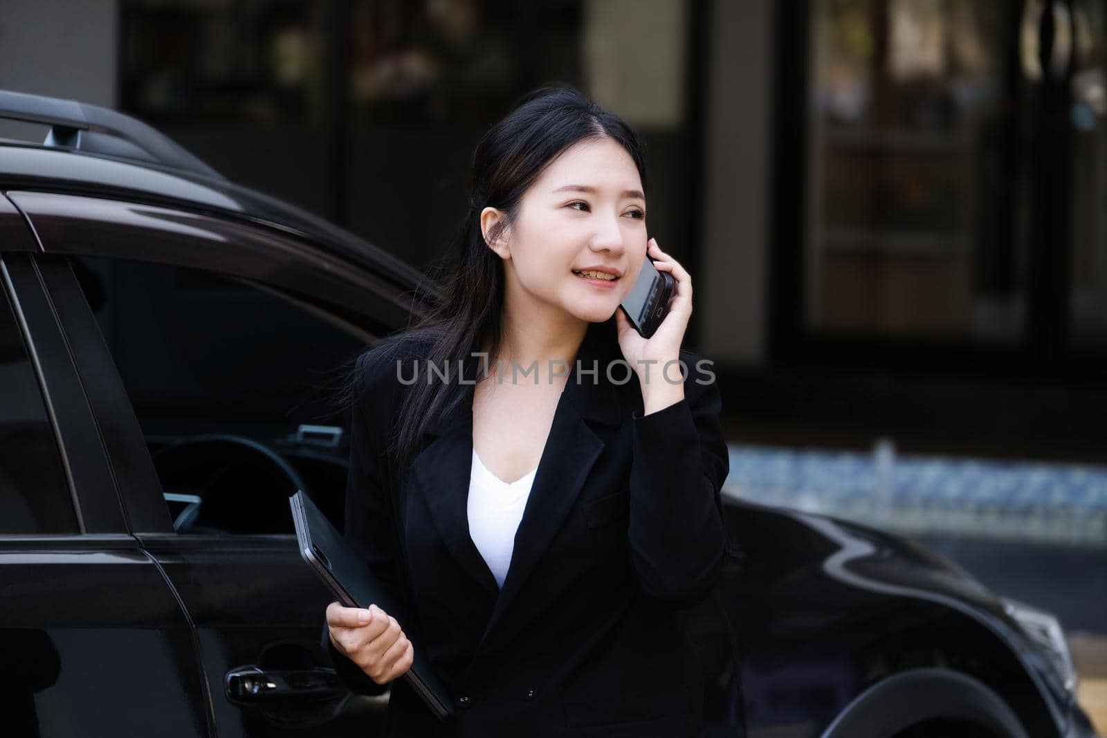 Asian businessmen, business owners, company presidents or female employees talking on the phone and holding a tablet are getting out of the car to attend a business plan meeting at the meeting