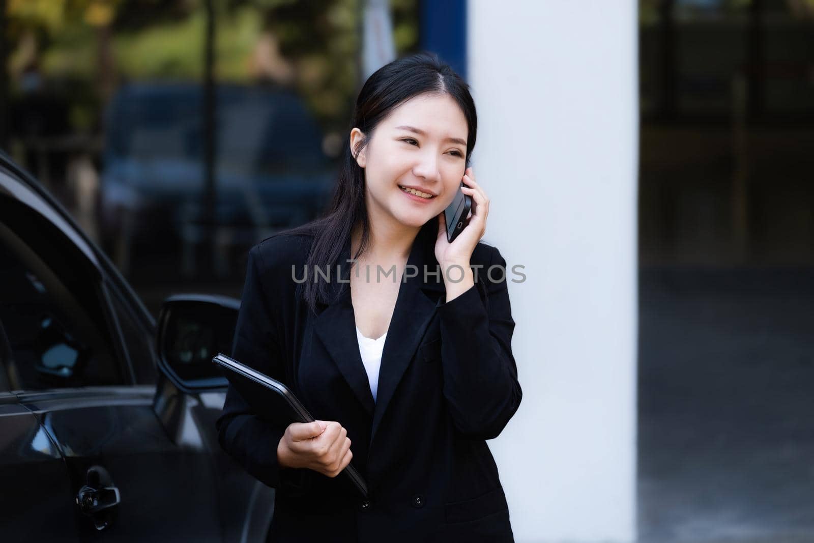 Asian businessmen, business owners, company presidents or female employees talking on the phone and holding a tablet are getting out of the car to attend a business plan meeting at the meeting