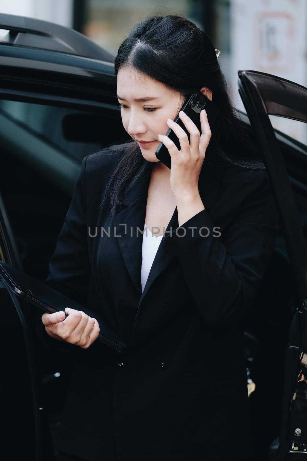 Asian businessmen, business owners, company presidents or female employees talking on the phone and holding a tablet are getting out of the car to attend a business plan meeting at the meeting