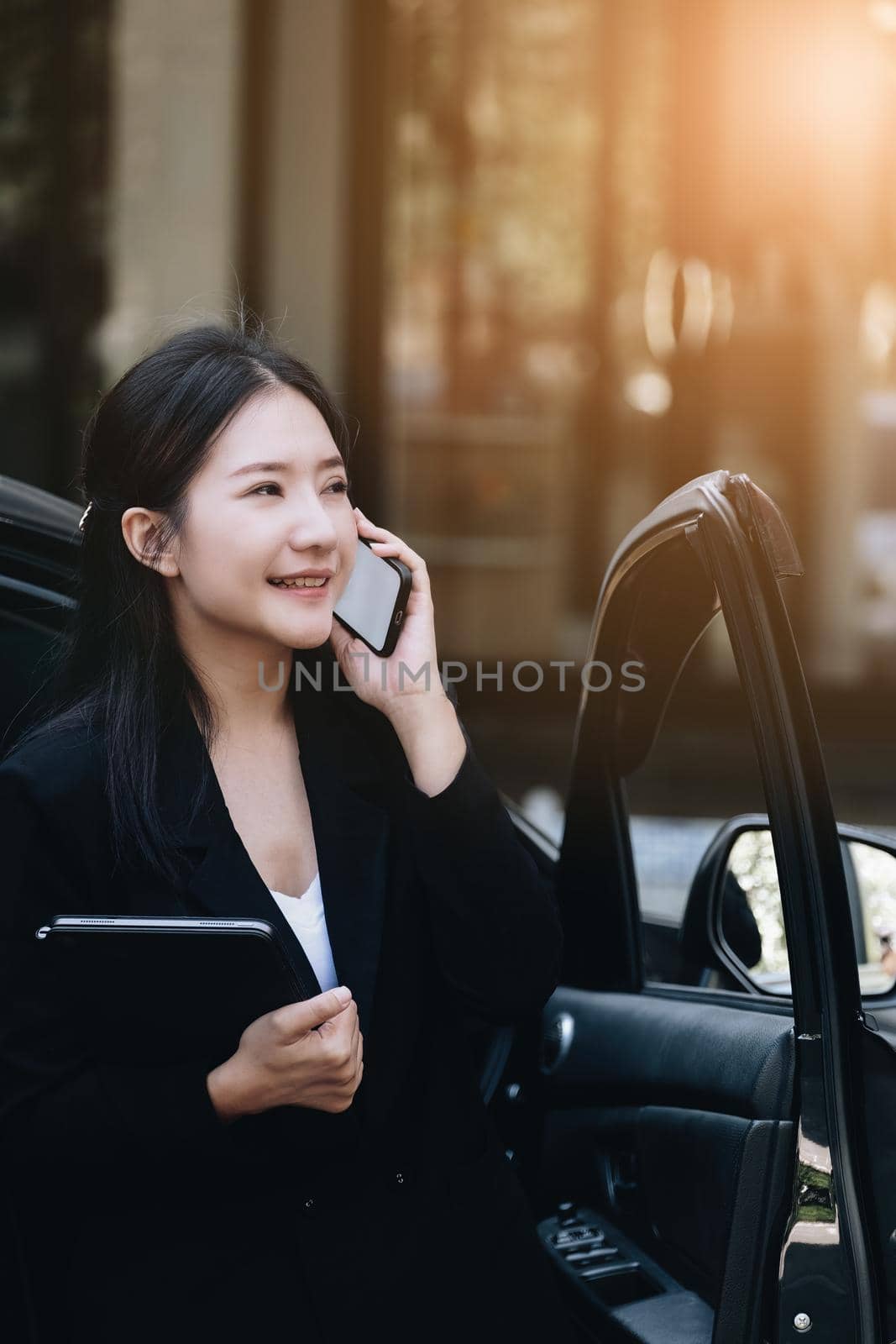 Asian businessmen, business owners, company presidents or female employees talking on the phone and holding a tablet are getting out of the car to attend a business plan meeting at the meeting