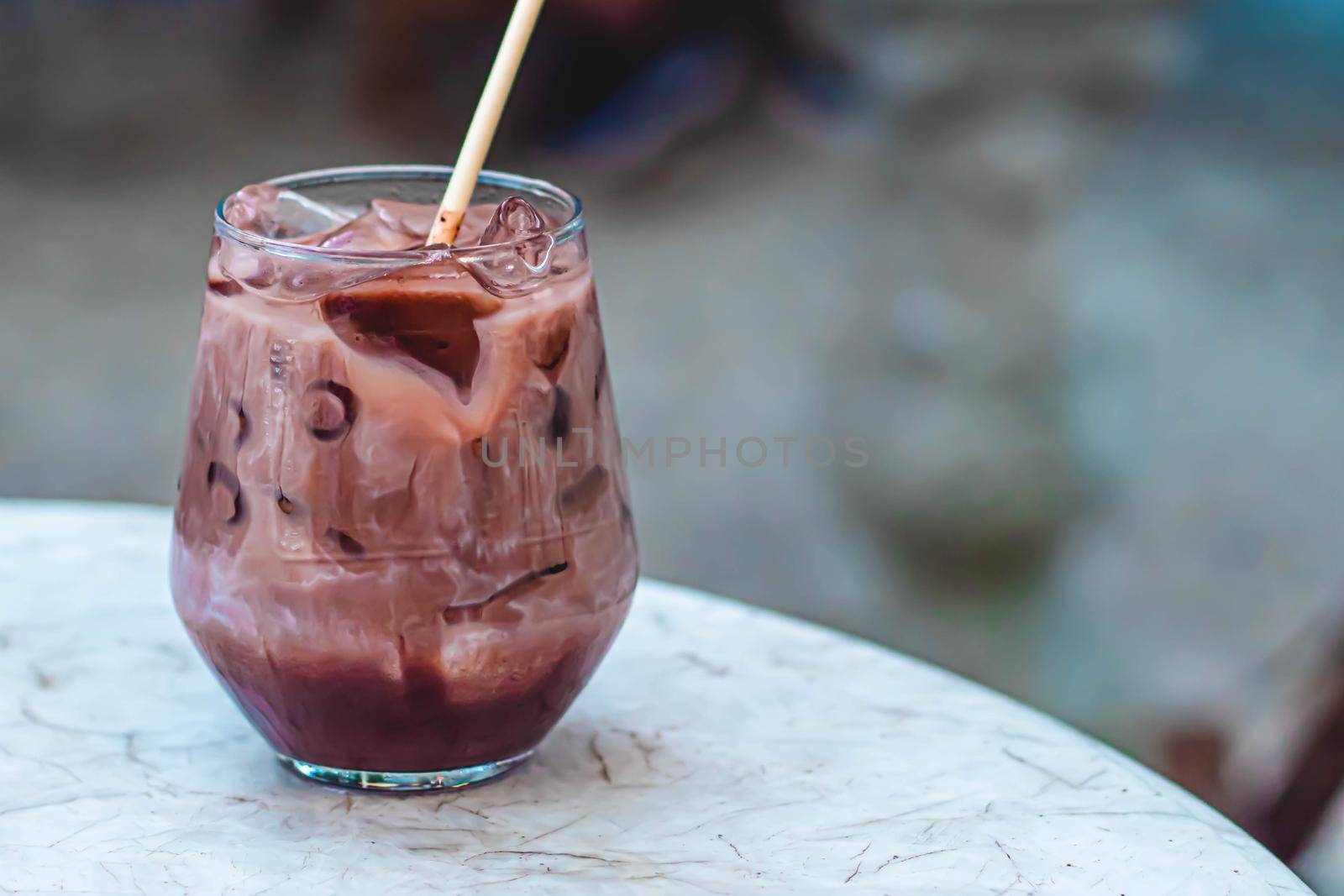 Close up summer refreshment drinks. Chilled iced chocolate cocoa. Chocolate powder and ice. In glasses, with tubes for drinking. Green leaves nature background. Close up of a glass of Iced Cocoa cool drink served on table. Iced chocolate drink in classic glass on green nature of summer background. Summer drink