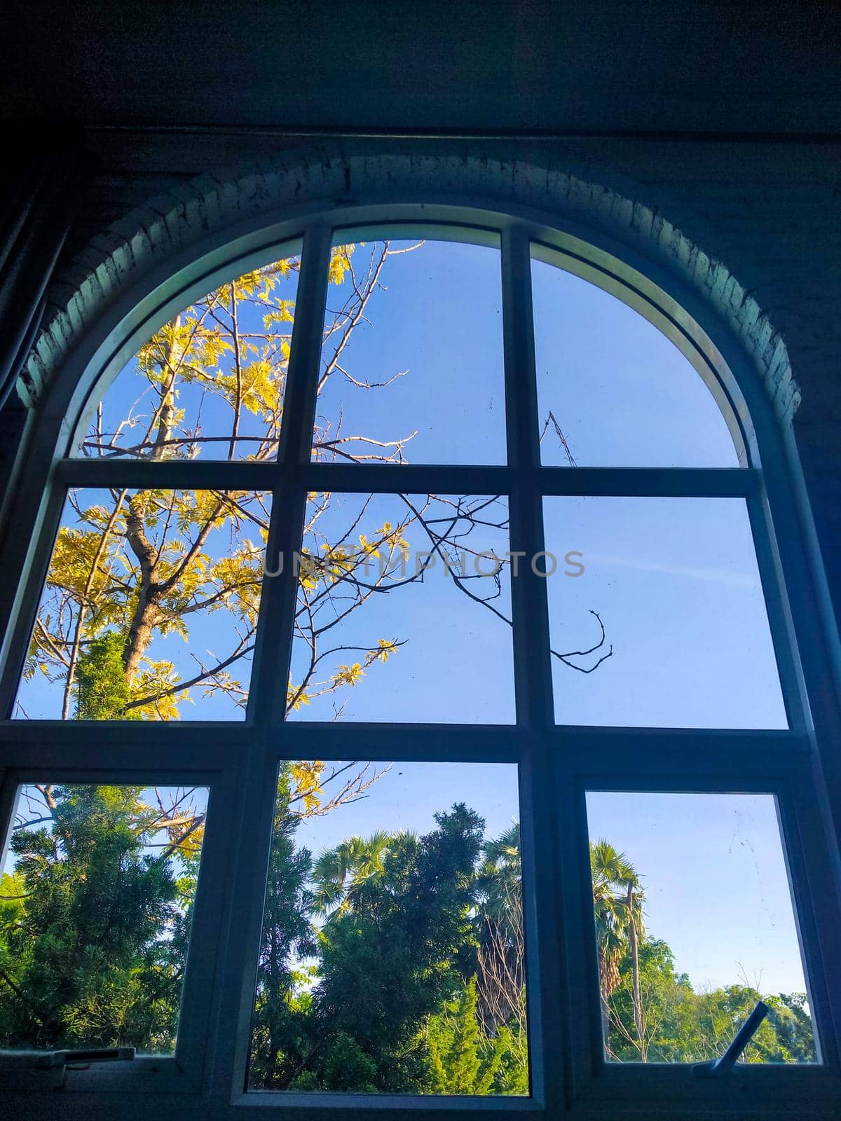 Arched window with view to autumnal landscape, bright sunshine. View through the window in autumn.