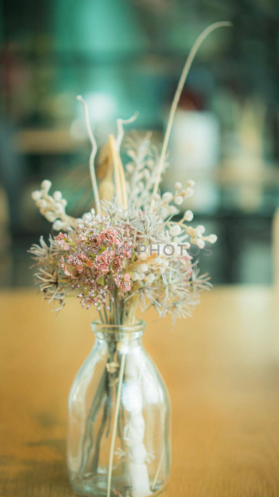 Bunch of dried flowers in a glass vase on wooden table. by Petrichor