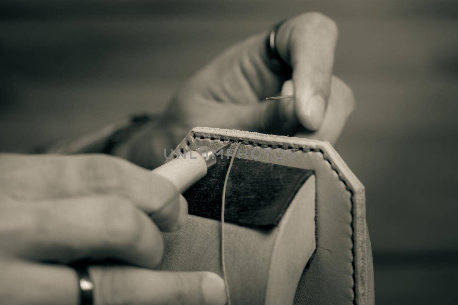 Sewing the vegetable tanned leather by hand. Leather and the craft tools. Monotone and shallow depth of field.