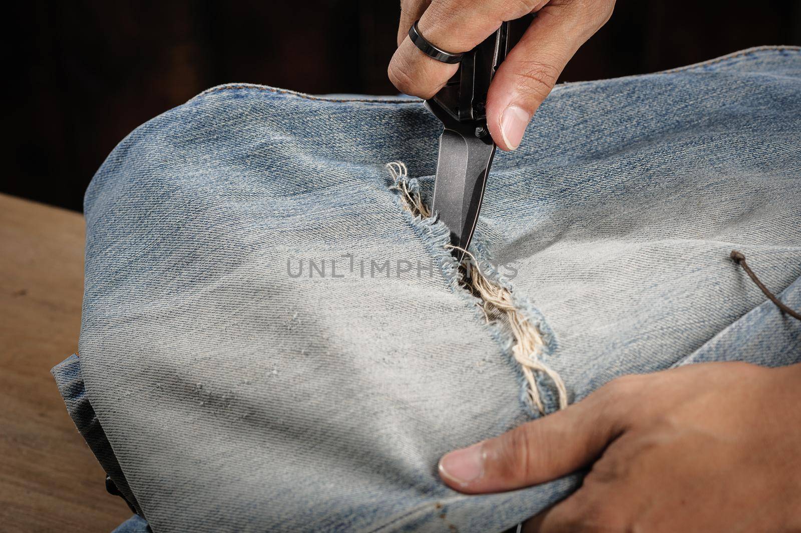 the man distressing jeans with folding knife.