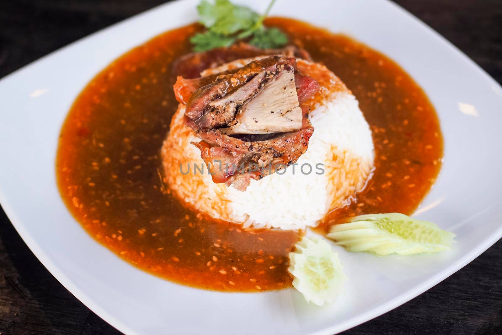 Red barbecued pork on rice, food serve with sweet curry and vegetable (cucumber, coriander) on white ceramic plate.