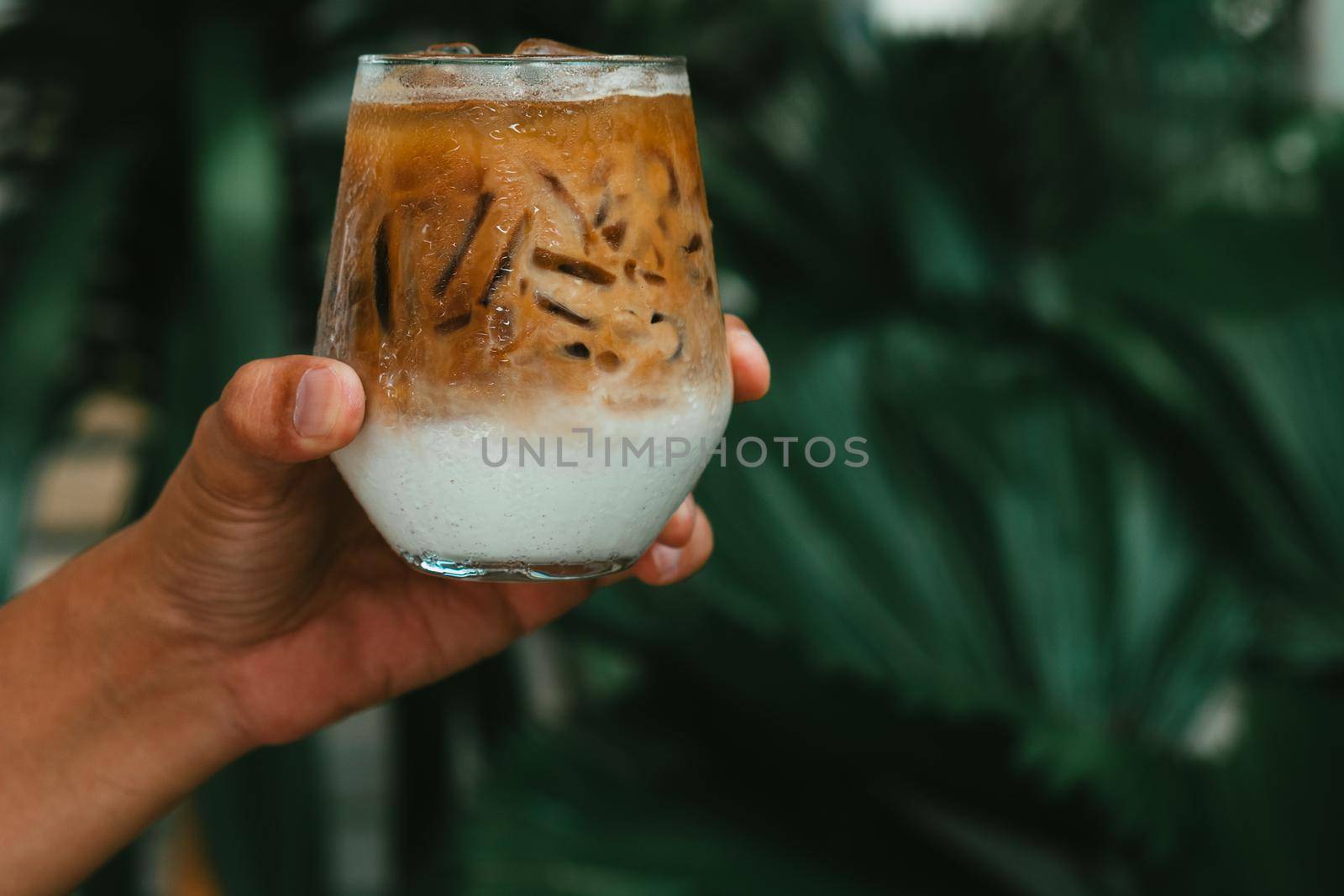 Hand hold iced latte coffee in a glass with cream on bottom . cold summer drink background
