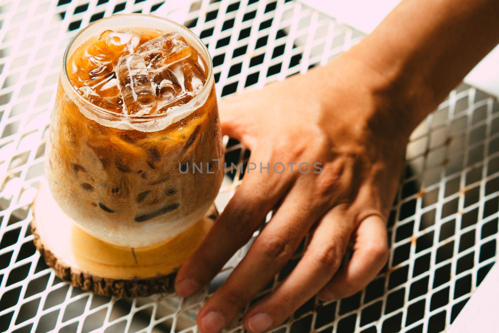 Hand hold iced latte coffee in a glass with cream on bottom . cold summer drink background