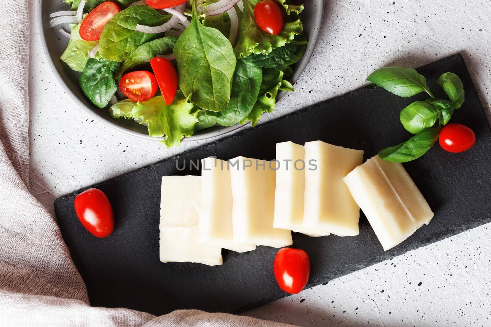 A piece of fresh sliced halloumi on a slate board with cherry tomatoes and spinach leaves. Preparing to cook cheese on the grill. Top view