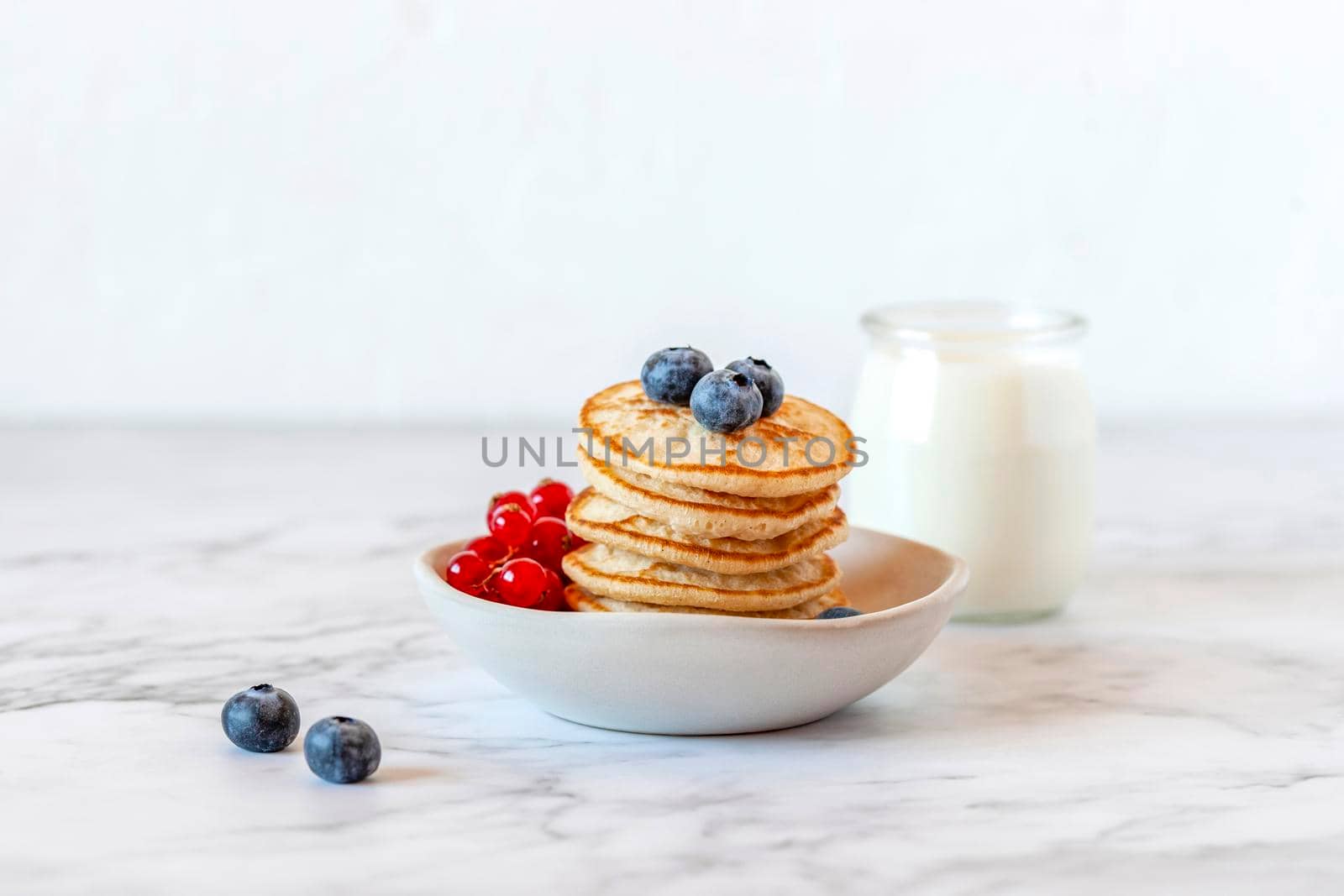 stack of homemade mini pancakes served with blueberries and red currants and joghurt, side view