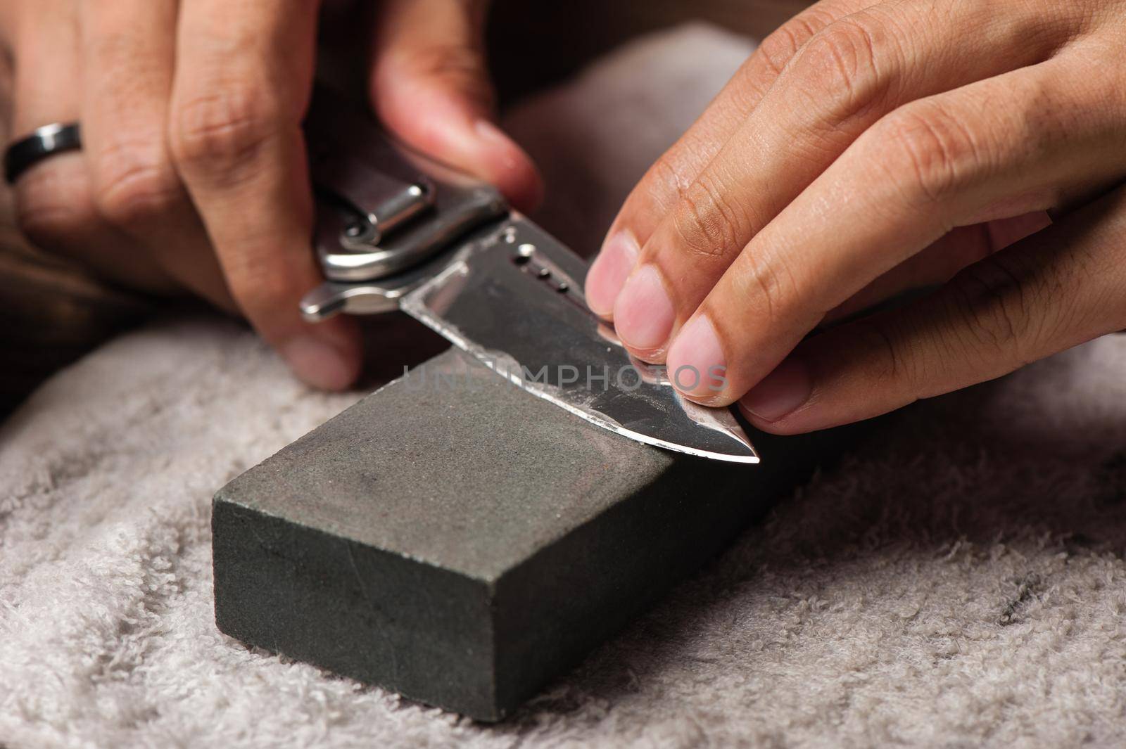 The man using whetstone to sharpening his pocket knife. Pocket knife care and maintenance concept.