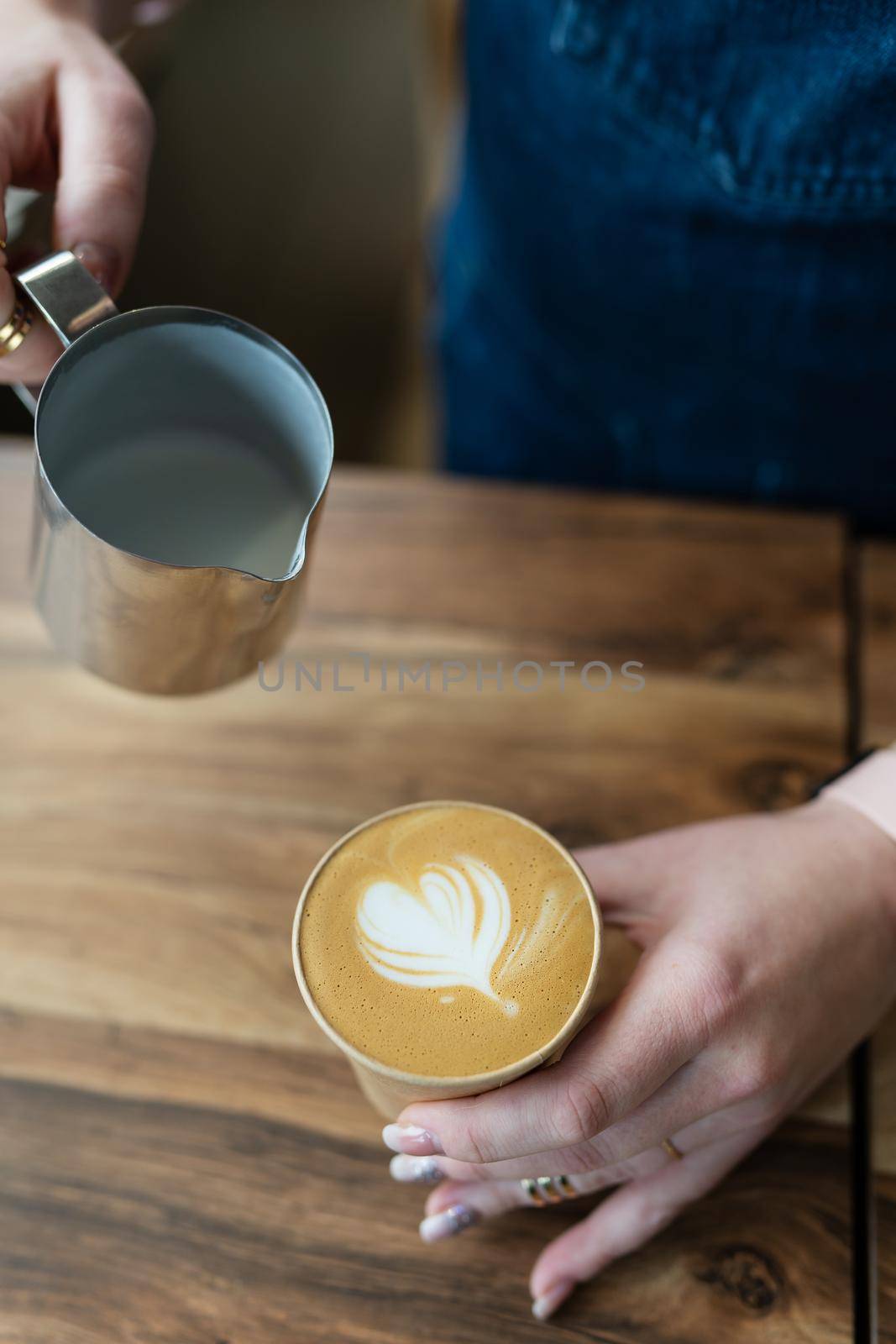 The process of making a barista cappuccino with a beautiful pattern in the form of a heart on the foam in an eco-craft glass. Coffee to go concept