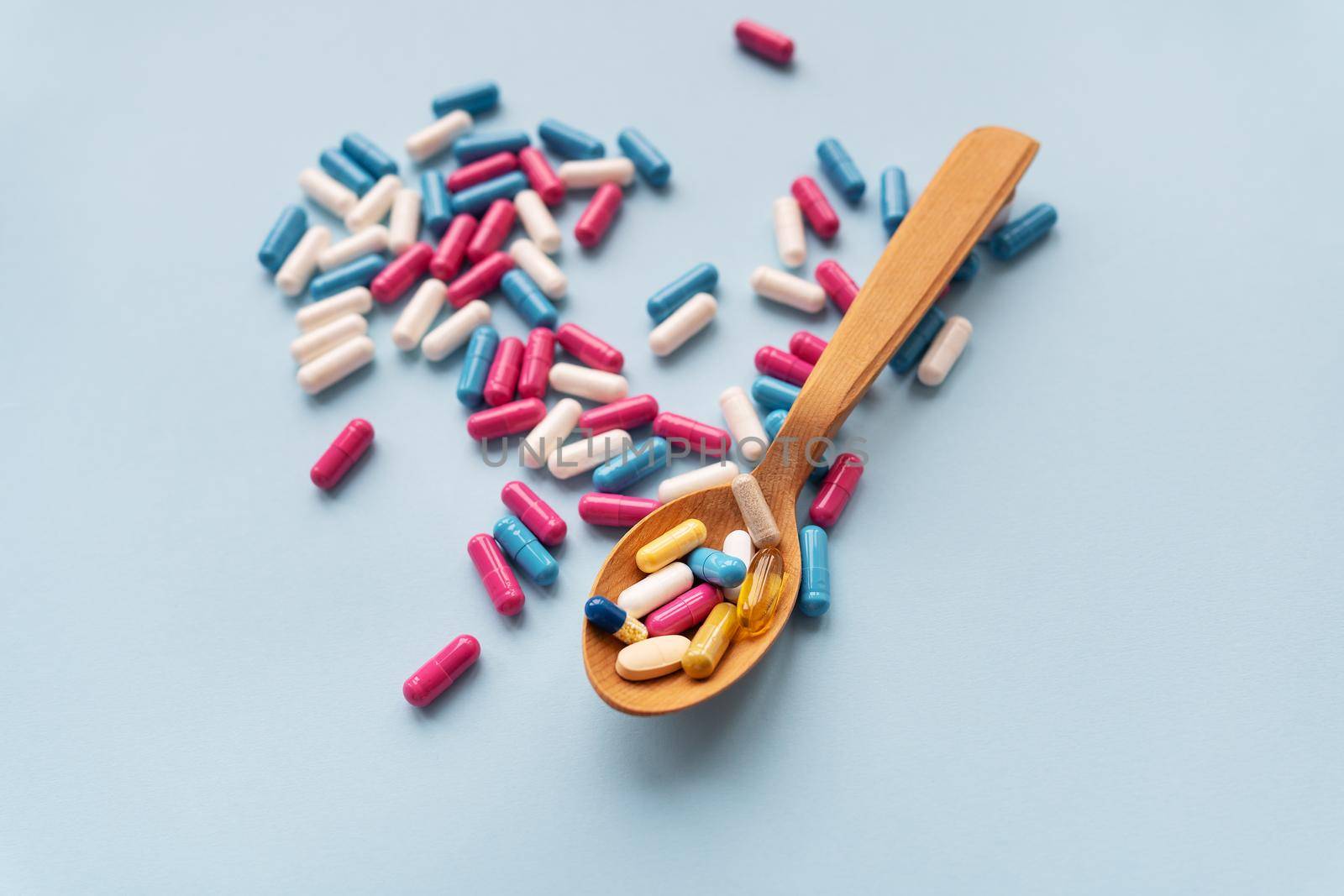 Various pills on a blue background together with a wooden spoon in which vitamins