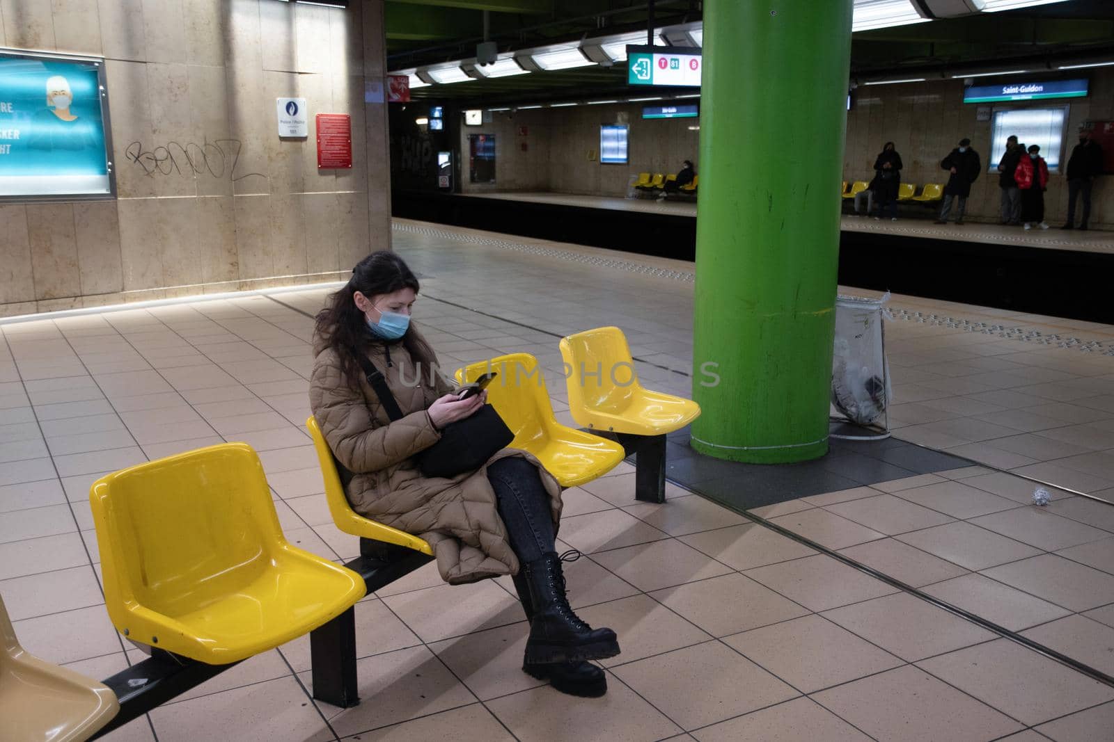 a young woman in a warm down jacket with green screen smartphone sits on an armchair in the waiting room in the subway watches the train and use social media, . High quality photo