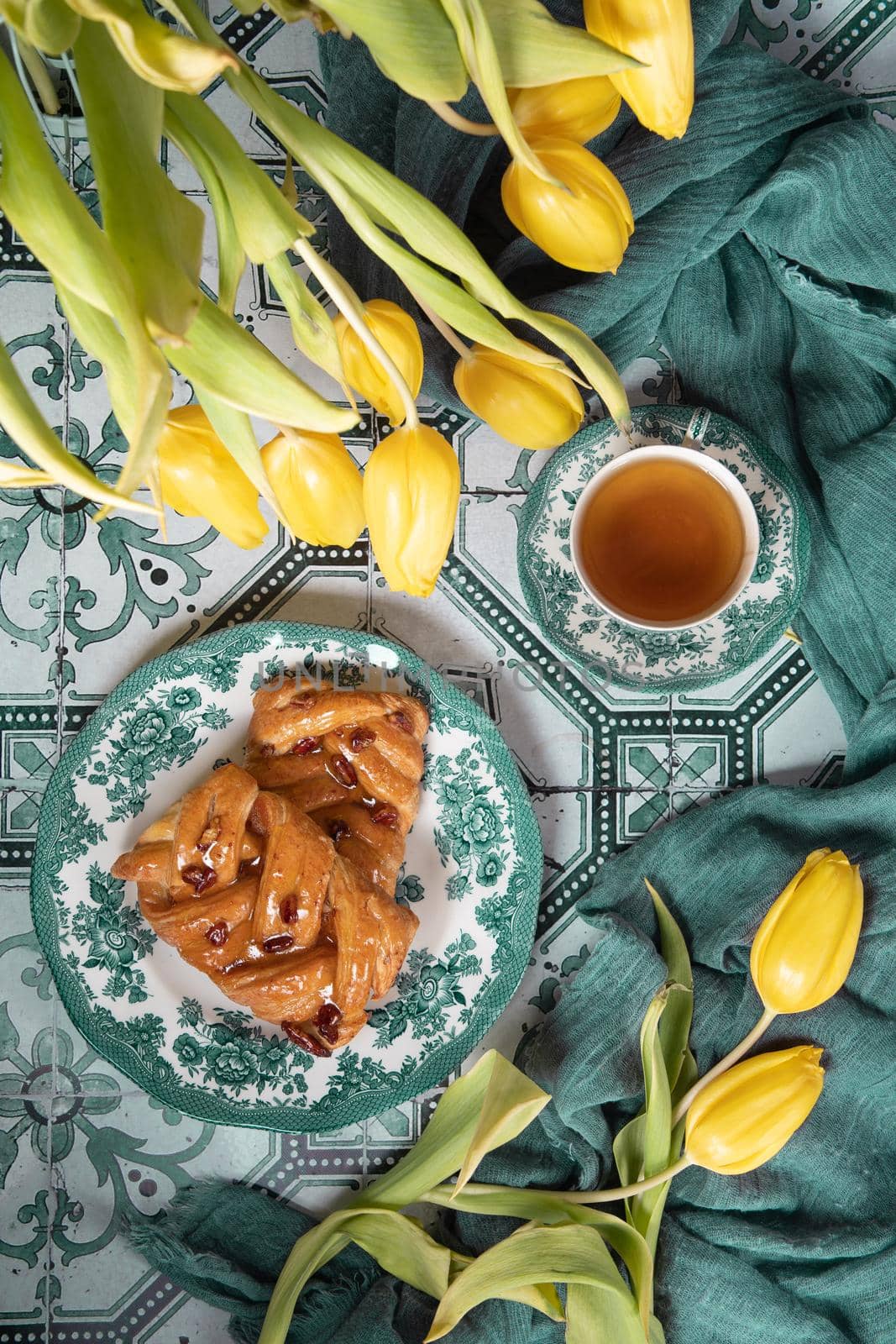 flat lay food, sweet puff, tea in a vintage porcelain cup and a stack of books, a bouquet of yellow withering tulips in a vase,. High quality photo