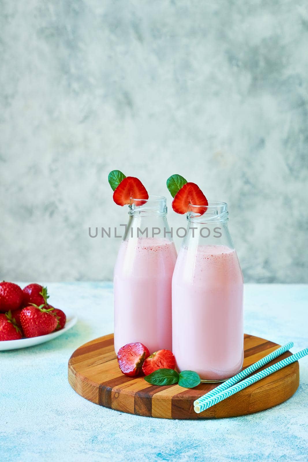 Strawberry smoothie or milkshake in glass jar with berries on wooden board on blue concrete background. Healthy summer drink