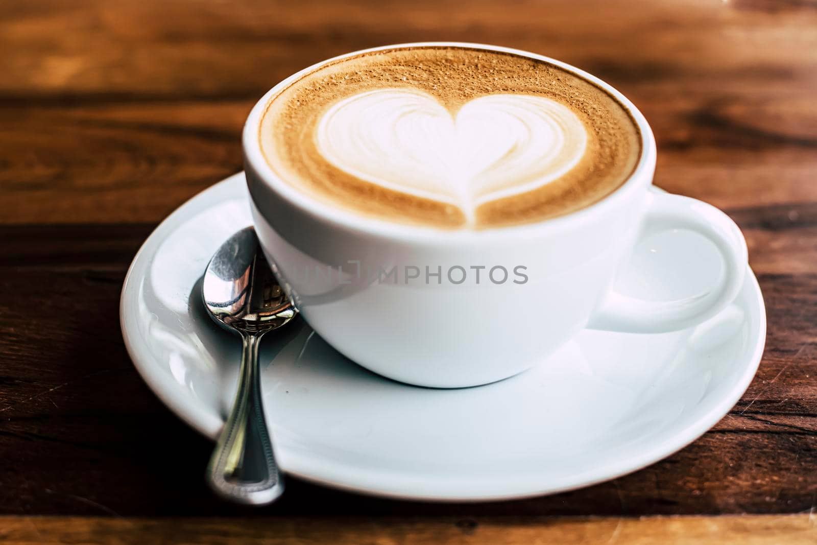 Cup of coffee latte with heart shape on old wooden background in the morning sunlight