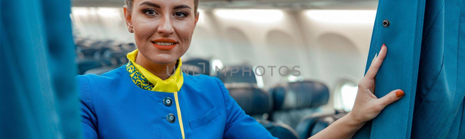 Joyful woman stewardess standing in passenger aircraft cabin by Yaroslav_astakhov