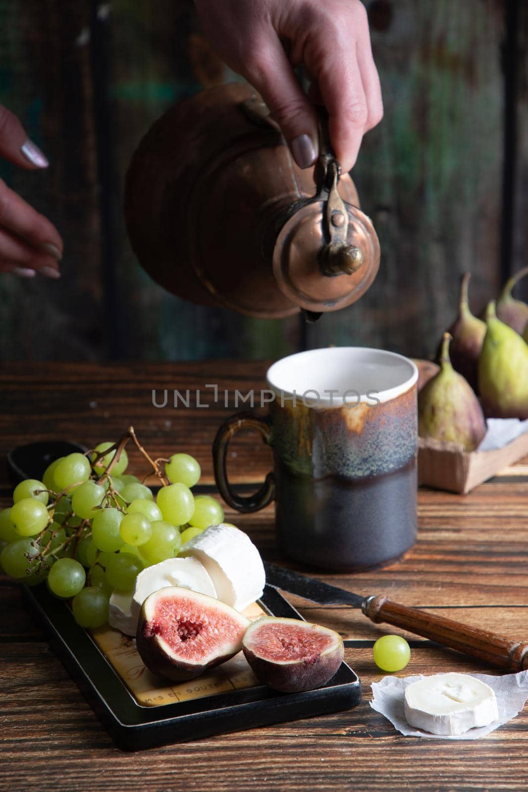 cheese plate with goat cheese, grapes and figs, copper teapot, angle view, healthy food, high-calorie breakfast. High quality photo