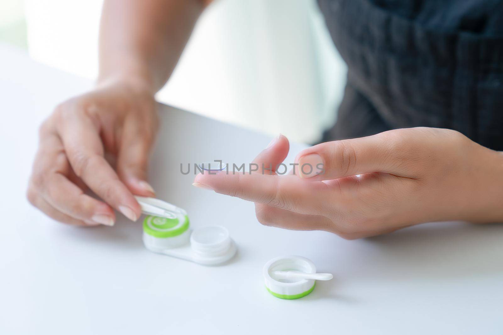 Woman puts it down contact lens on her index finger with tweezers. Close-up, side view by Laguna781