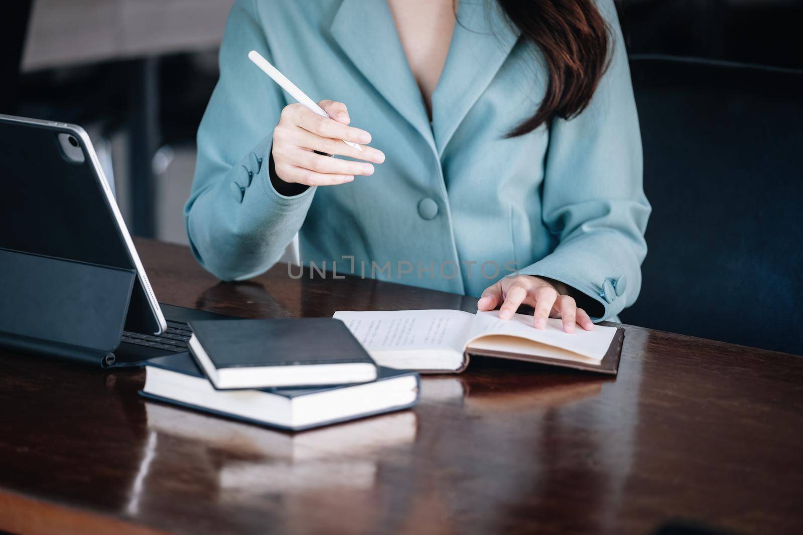 A female entrepreneur or businesswoman showing a smiling face while reading a book developing financial and investing strategies and operating a computer tablet working on a wooden table. by Manastrong