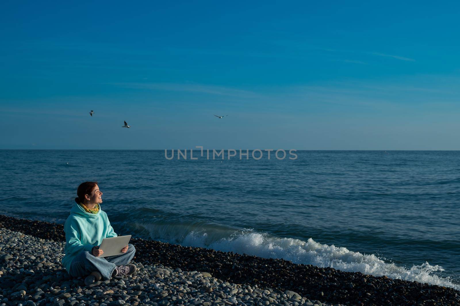 Happy caucasian woman working on a laptop while sitting on a pebble beach