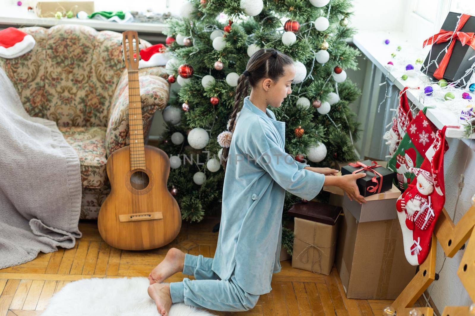 Merry Christmas and Happy Holidays Cute little child girl is decorating the Christmas tree indoors