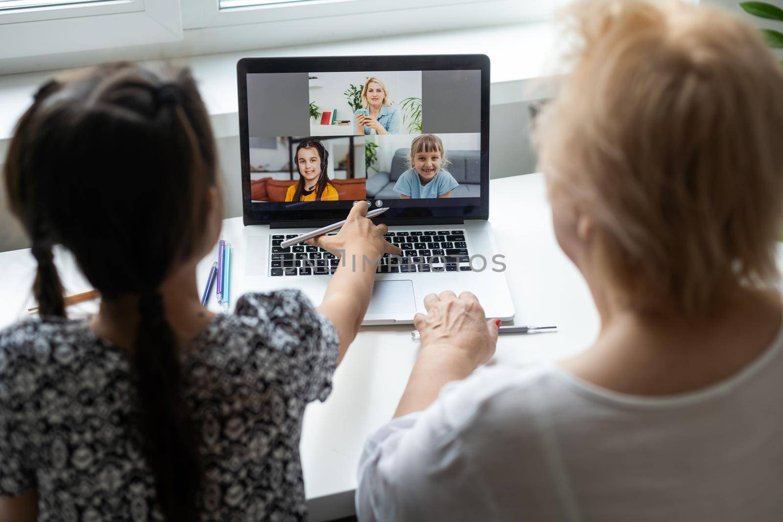 Portrait of happy grandmother and little granddaughter making video conference on pc sitting at table, waving hands at screen, greeting somebody, chatting with parents, enjoying online communication. by Andelov13