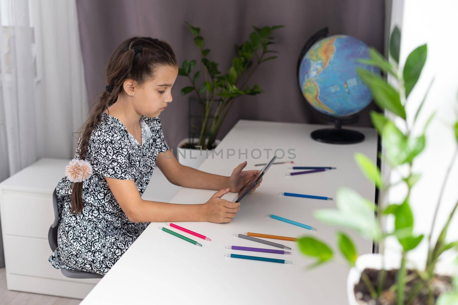 Back to school. Happy little schoolgirl sitting at her Desk. The girl does her homework using a tablet computer. online education.