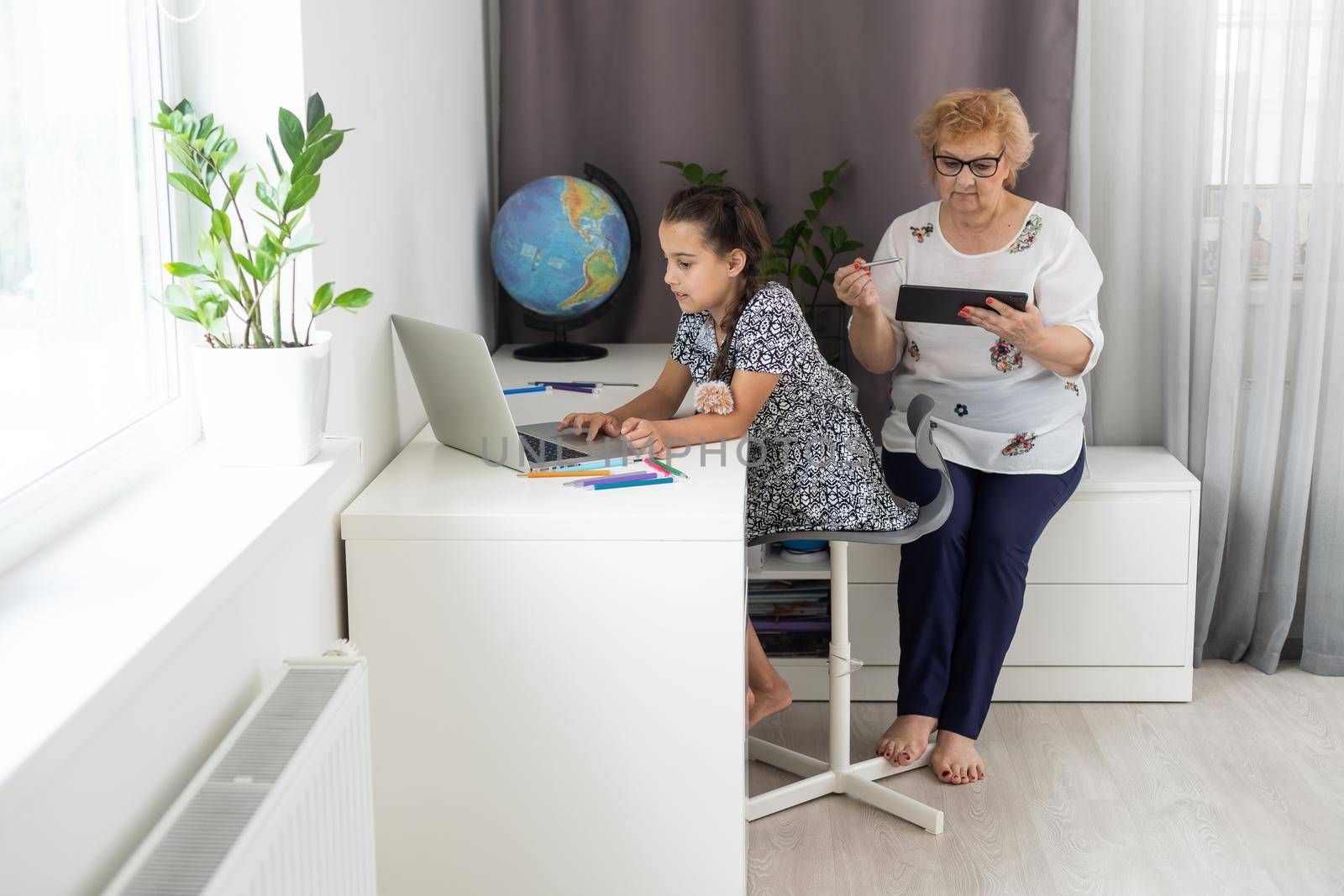 Older woman grandma and little girl grandkid with homework remote study. Attentive mature old female tutor give private lesson to small child pupil by Andelov13