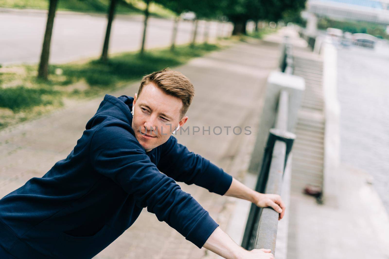 Young tired fitness man runner relax and stretching after exercise run outdoors in city urban street. Healthy lifestyle and sport concept. Tired after workout