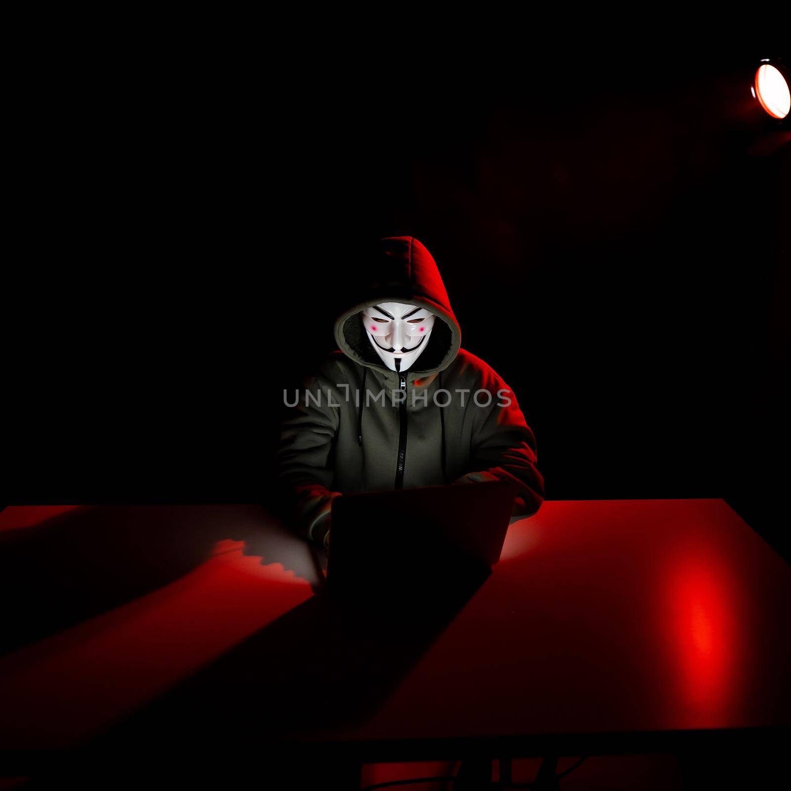 June 5, 2022 Novosibirsk, Russia: Anonymous in a hood is typing on a laptop in the dark in red light