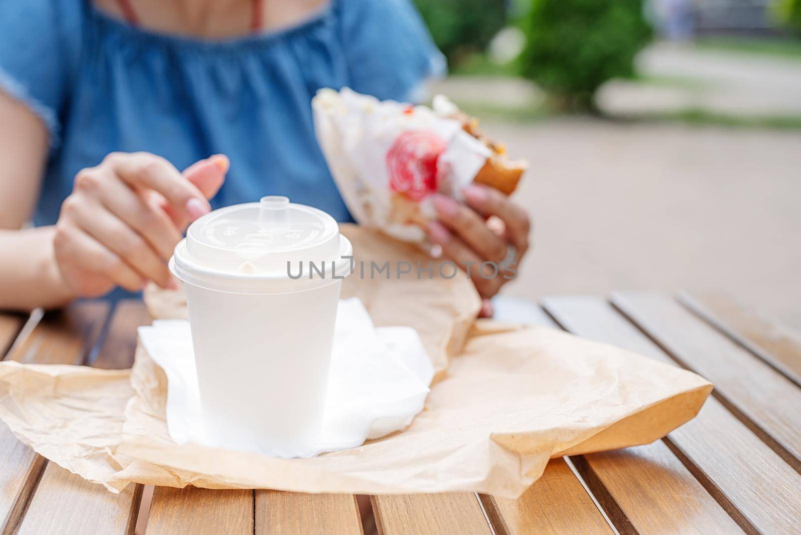 Summer vacation, street food eating. closeup of woman eating fast food in street cafe, mockup white coffee cup, focus on foreground