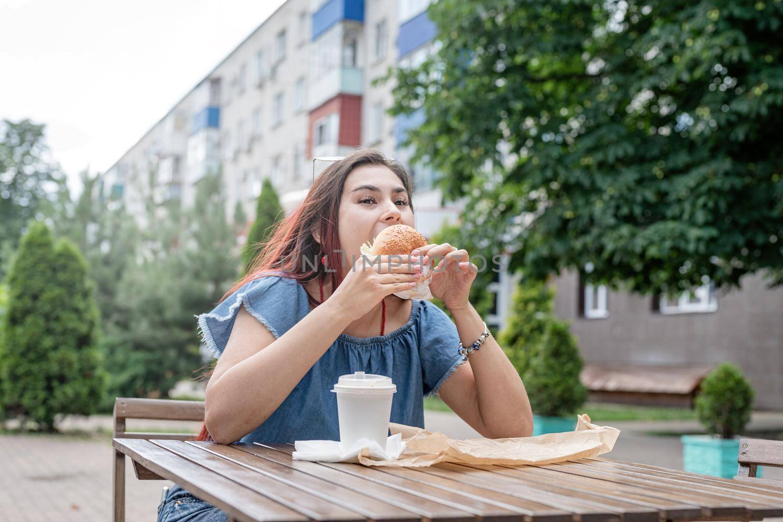 Stylish millennial woman eating burger at street cafe in summer by Desperada