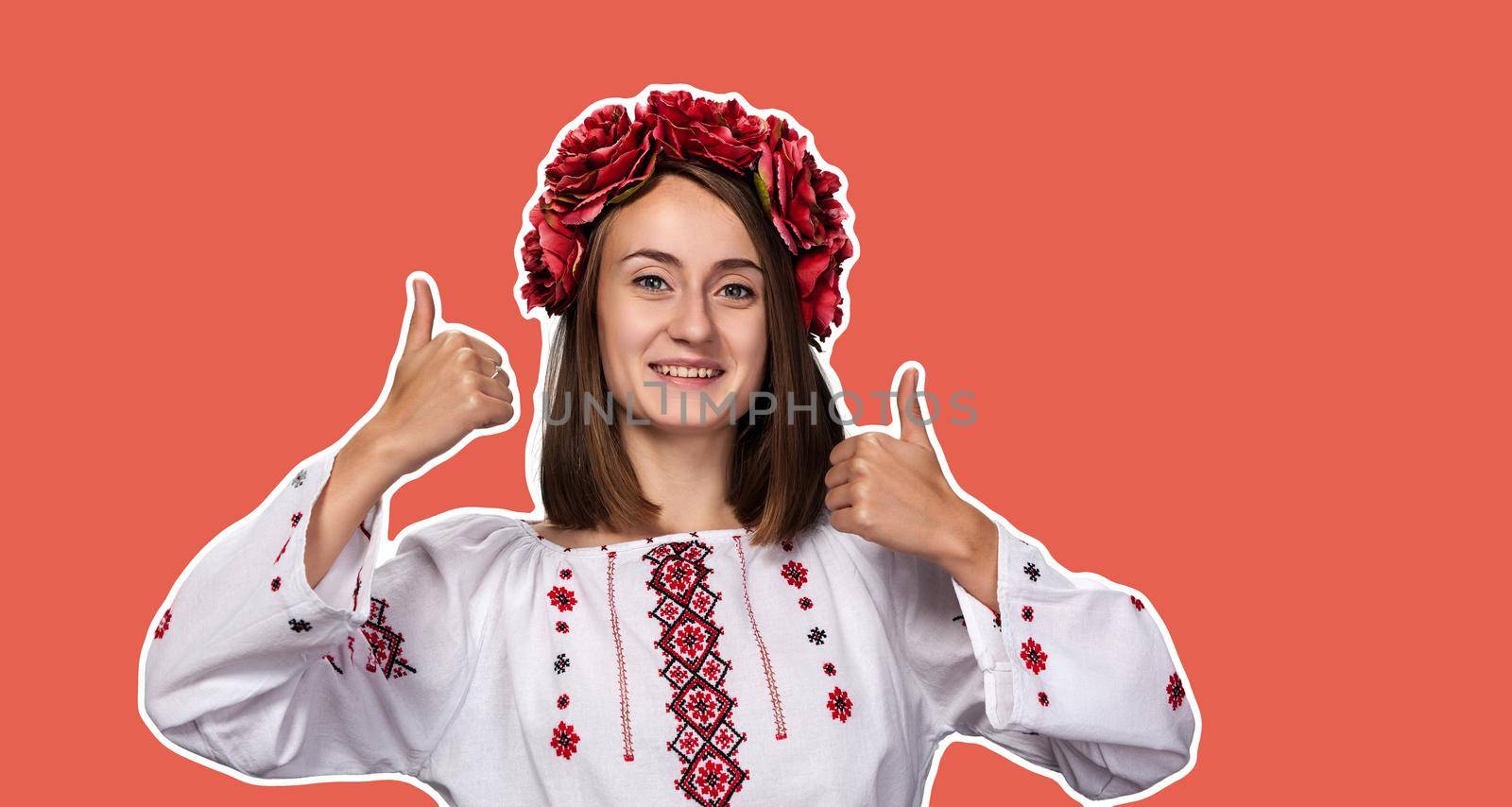 Happy young girl in the ukrainian national suit smiles and shows sign ok thumb up. Magazine style collage with copy space and trendy coral color background
