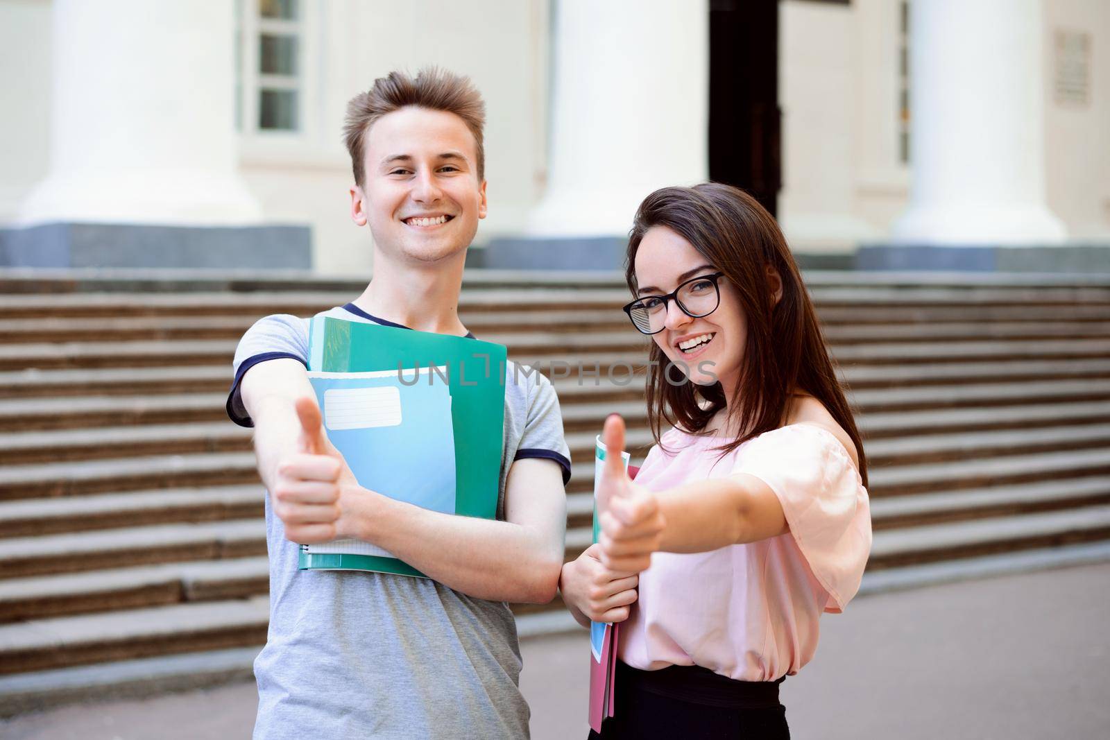 Happy students looking at camera showing thumbs up outside an university campus