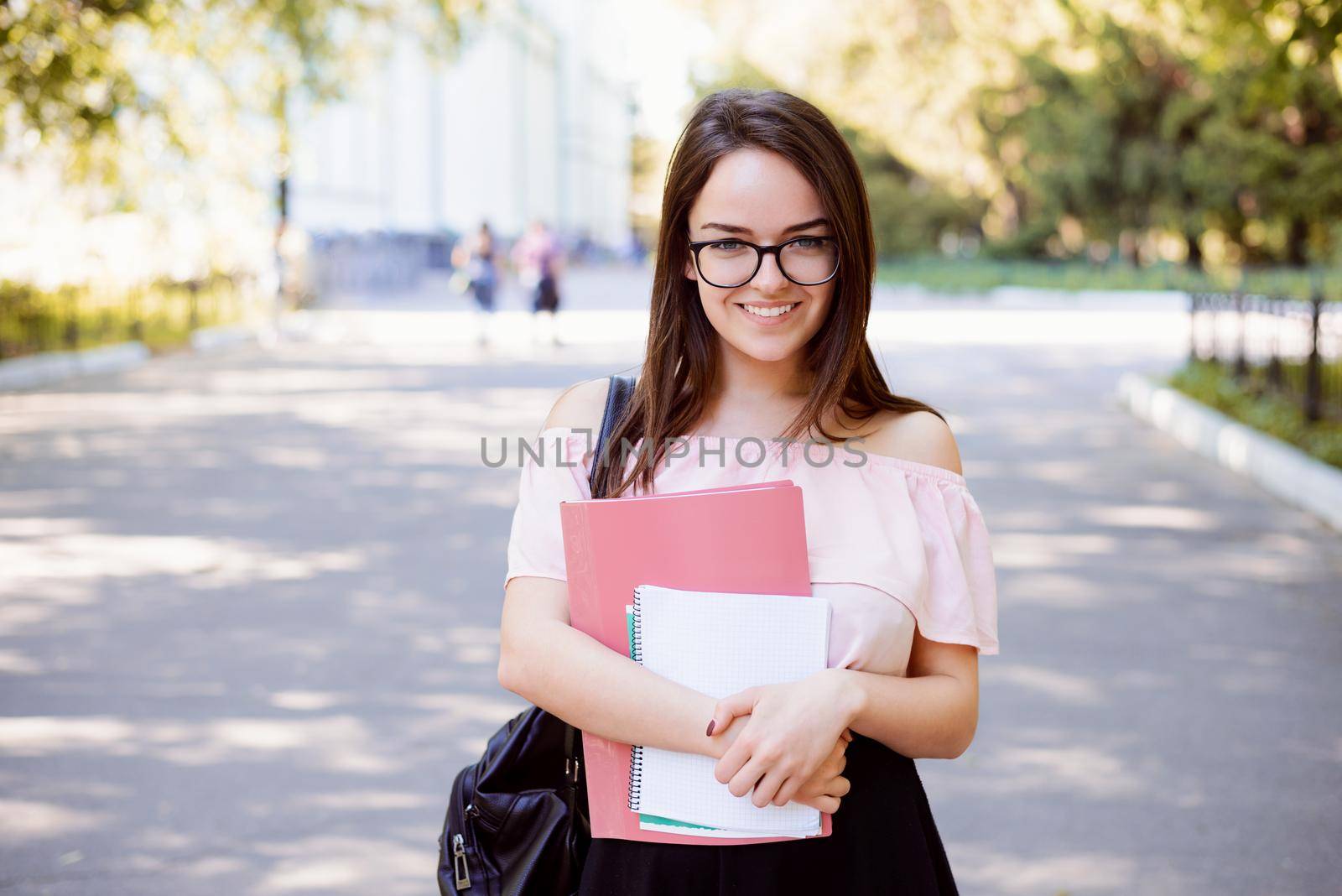 Cheerful girl student with books and notes goes from university after classes happy to have good day of studying