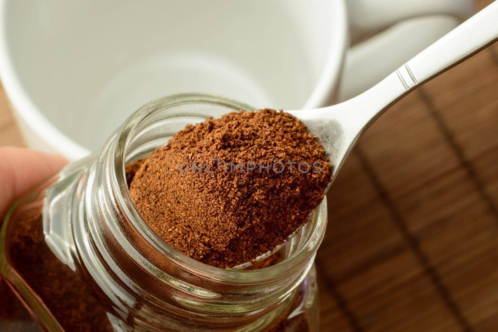 Man`s hand taking some ground coffee from coffee jar