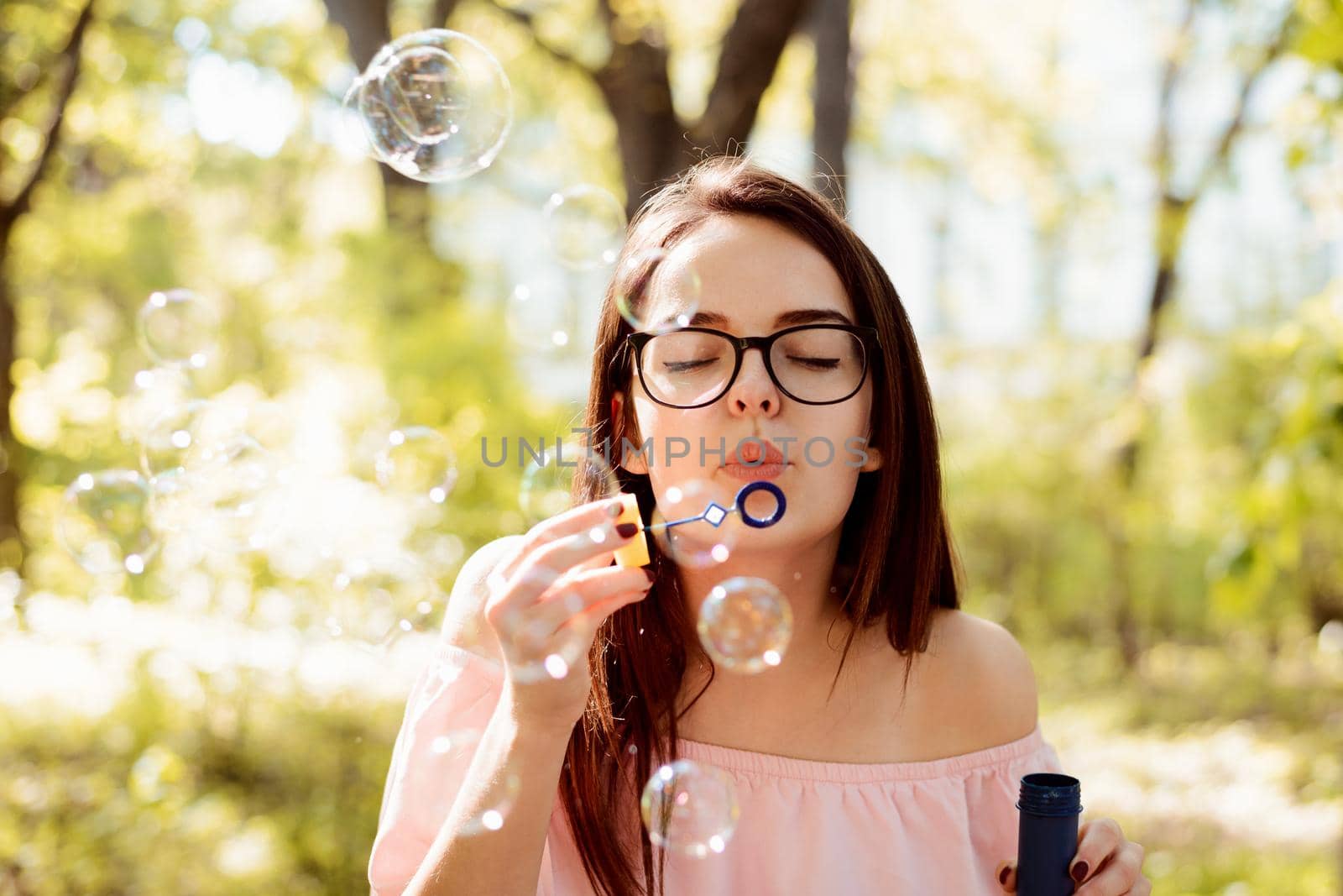 Beautiful young brunette girl blowing soap bubbles outdoors
