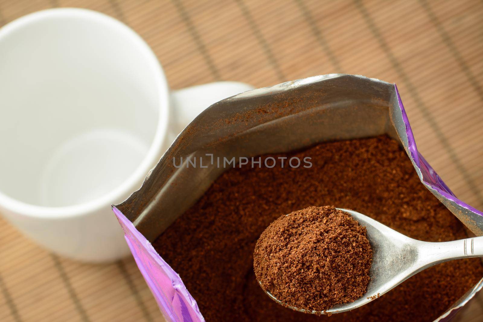 Spoon with some ground coffee against a big pack of coffee near the empty cup