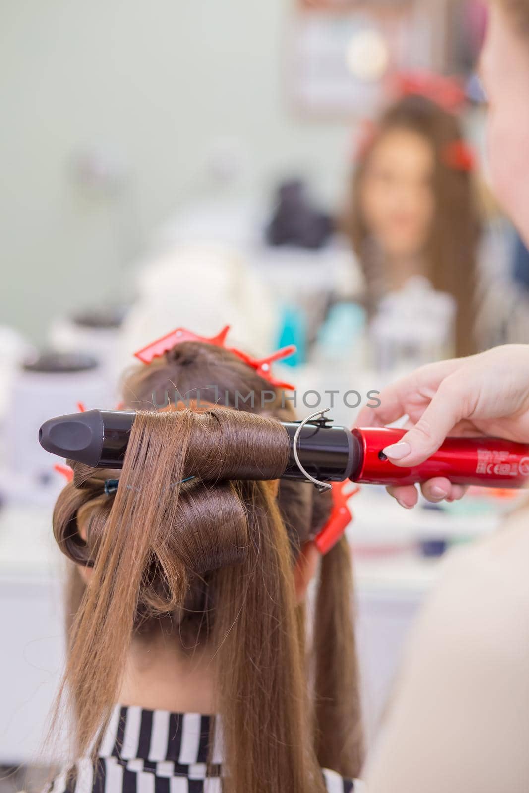 The master's hand curls a lock of hair on a woman's head with tongs close-up. The hairdresser makes a hairstyle for a young woman. Barber shop, business concept. Beauty salon, hair care.