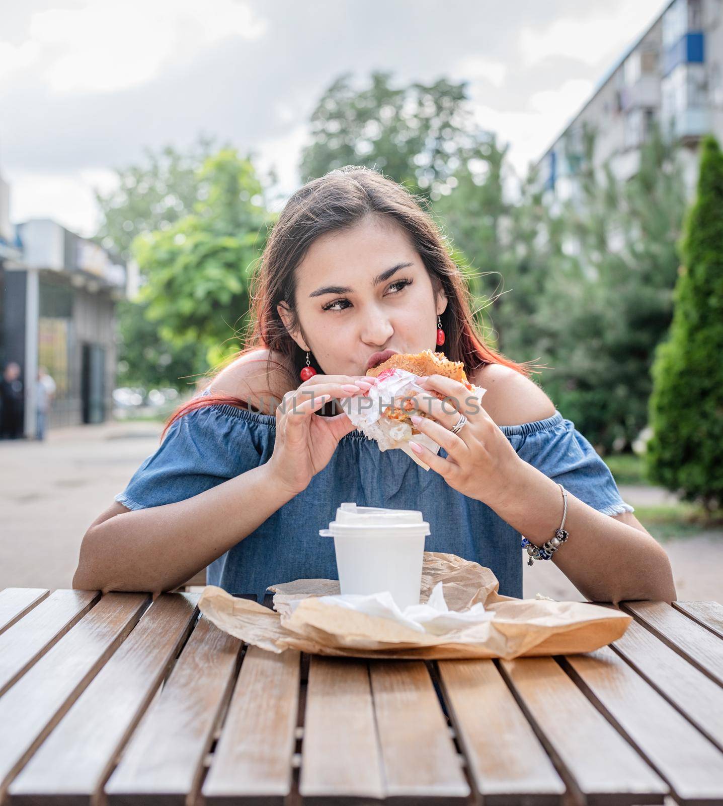 Stylish millennial woman eating burger at street cafe in summer by Desperada