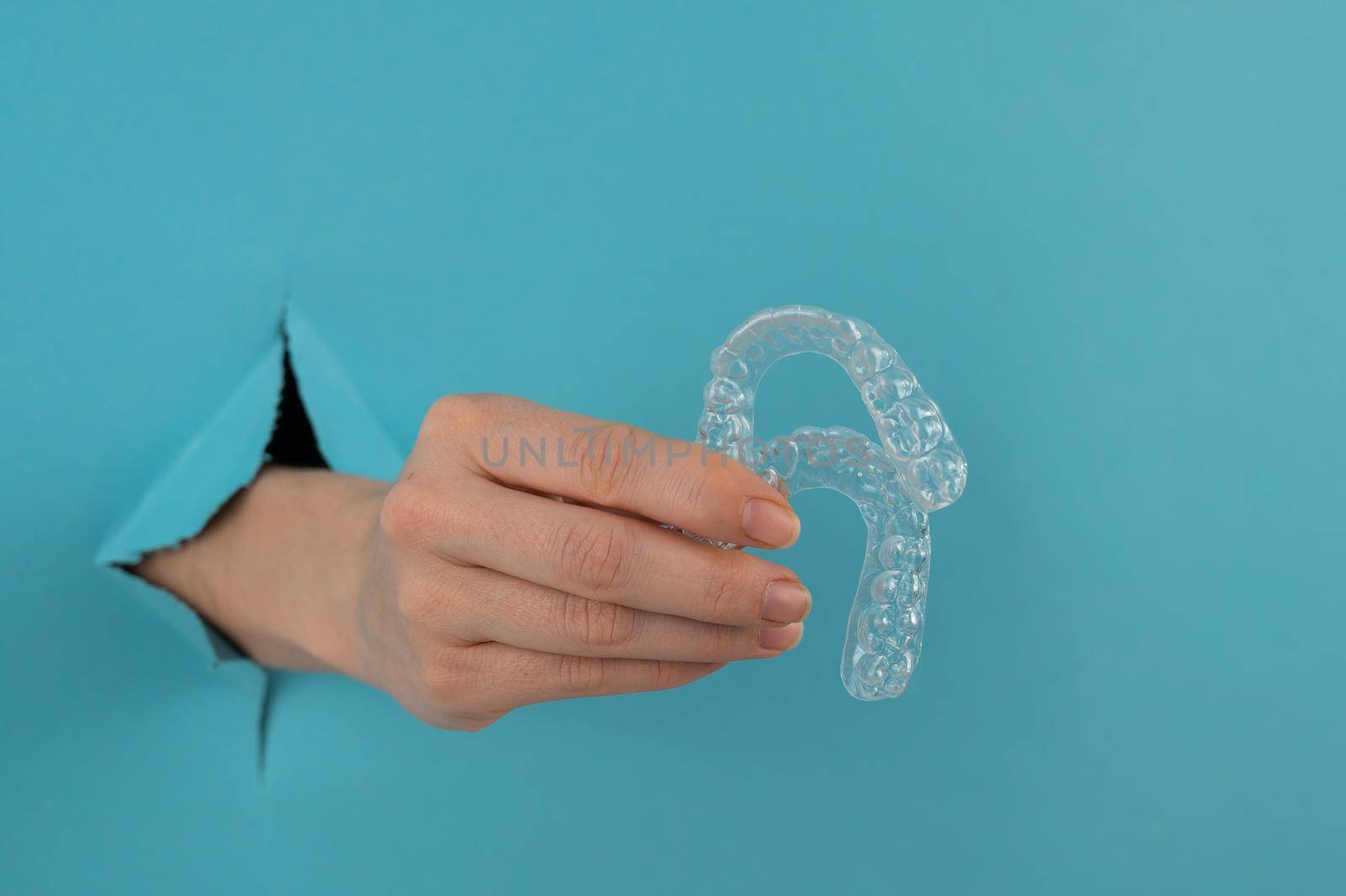 A female hand sticking out of a hole from a blue background holds removable night retainers