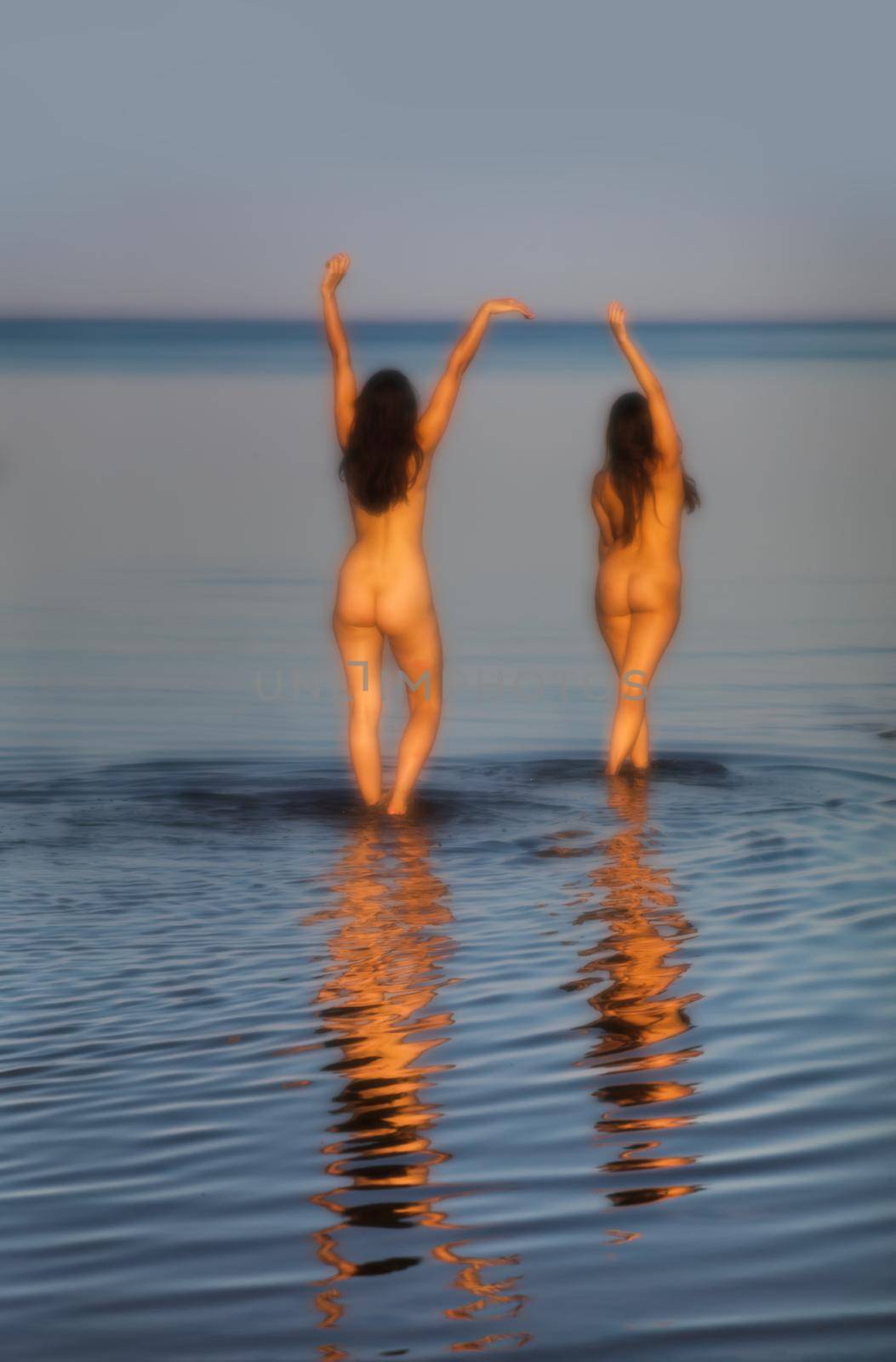 Soft focus image of a beautiful naked girl outdoors enjoying nature. Two young nude women posing on sea background. Sexy naked brunettes enjoying summer time outdoors. View from the back