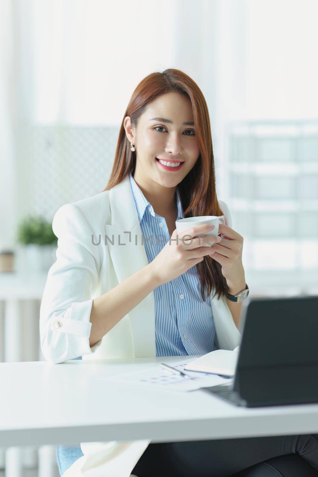 Portrait of an Asian businesswoman or business owner taking a coffee break while working in the office by Manastrong