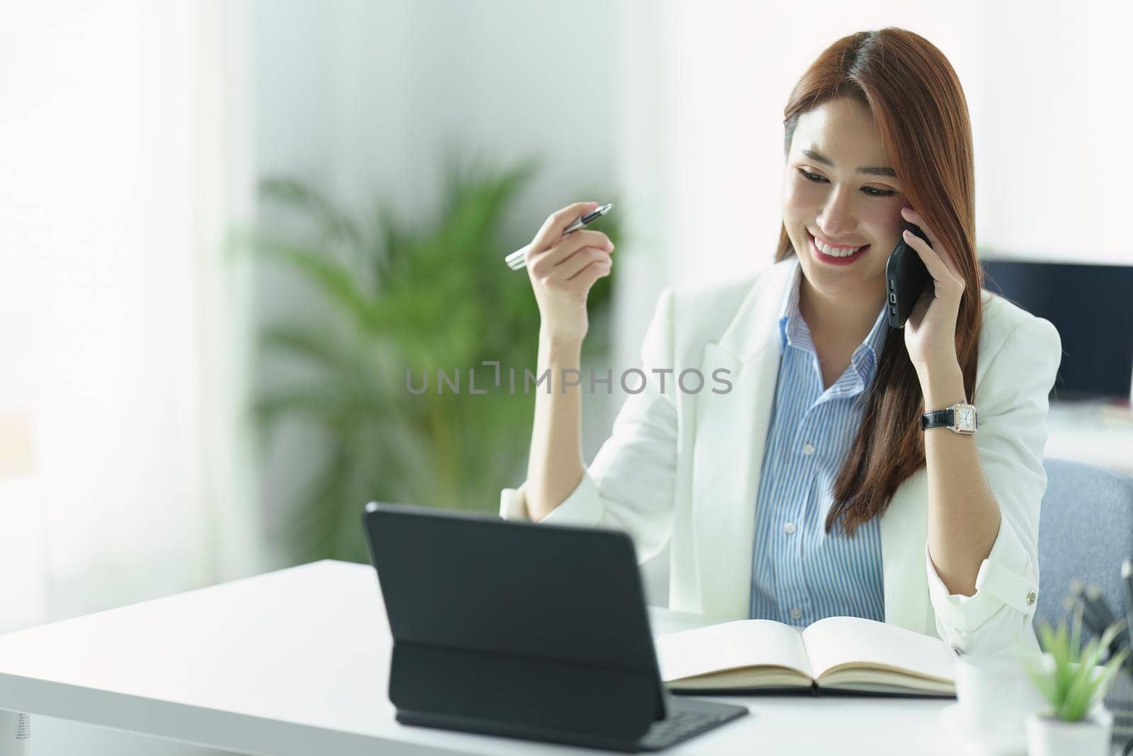 Portrait of an Asian businesswoman or business owner smiling and talking on a mobile phone in the office by Manastrong
