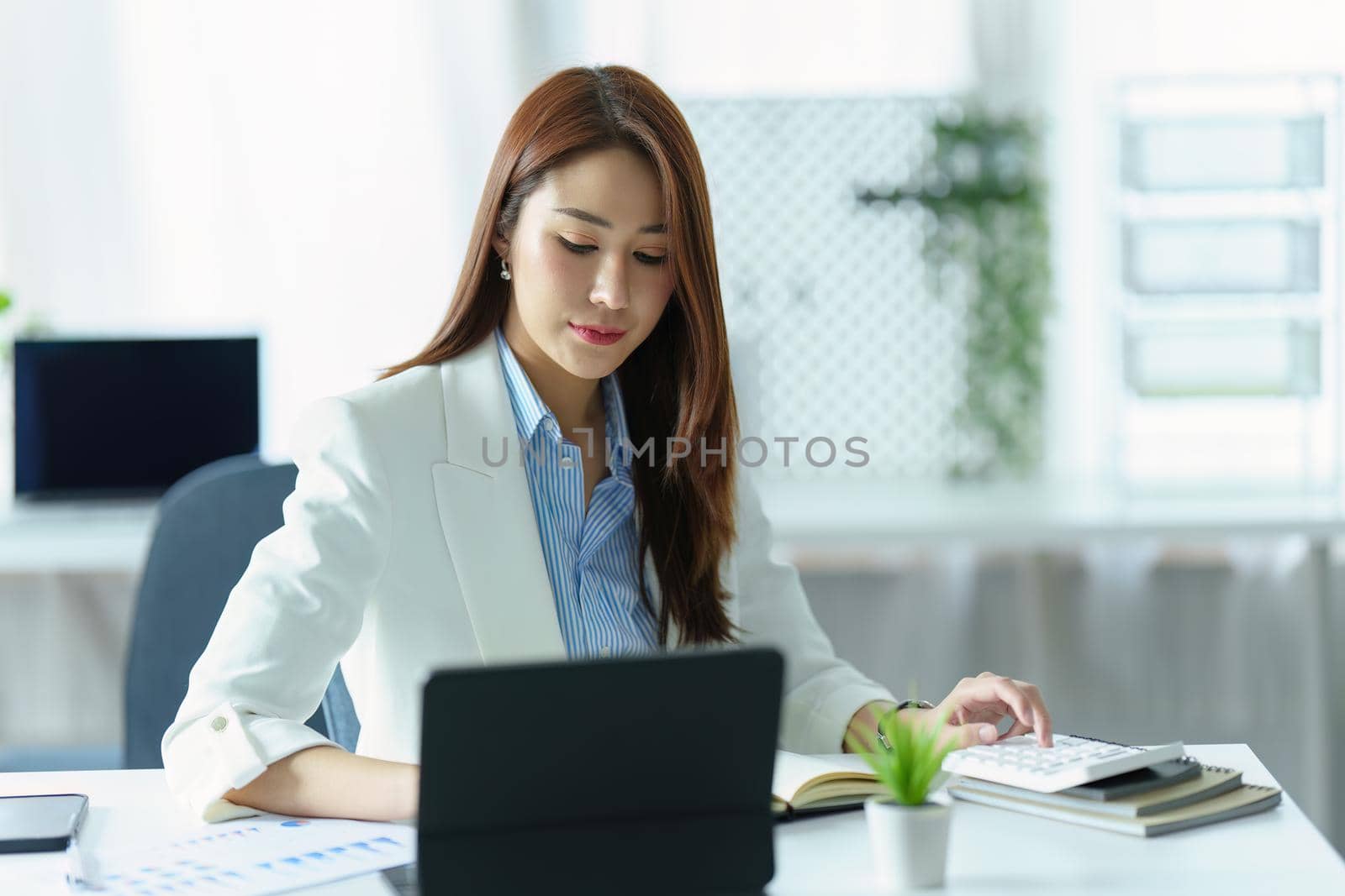 portrait of Asian businesswoman or business owner using Tablet computer, budget calculator and office marketing planner.