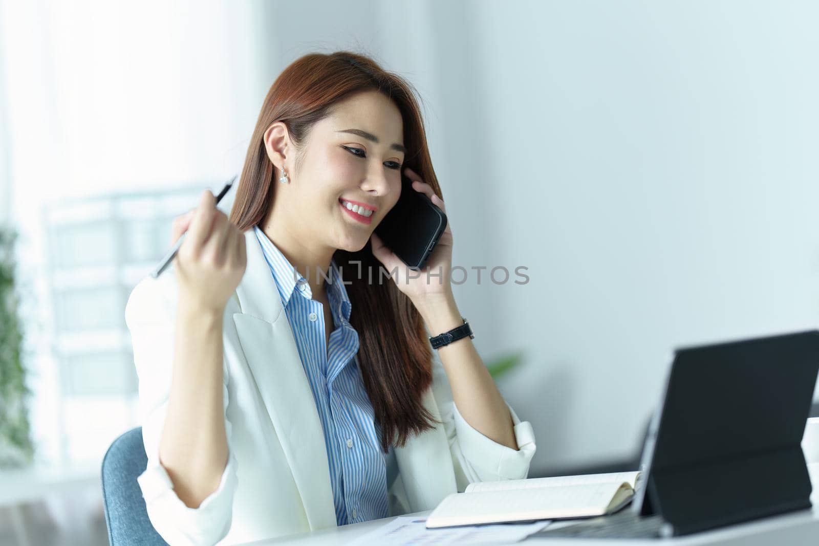 Portrait of an Asian businesswoman or business owner smiling and talking on a mobile phone in the office.
