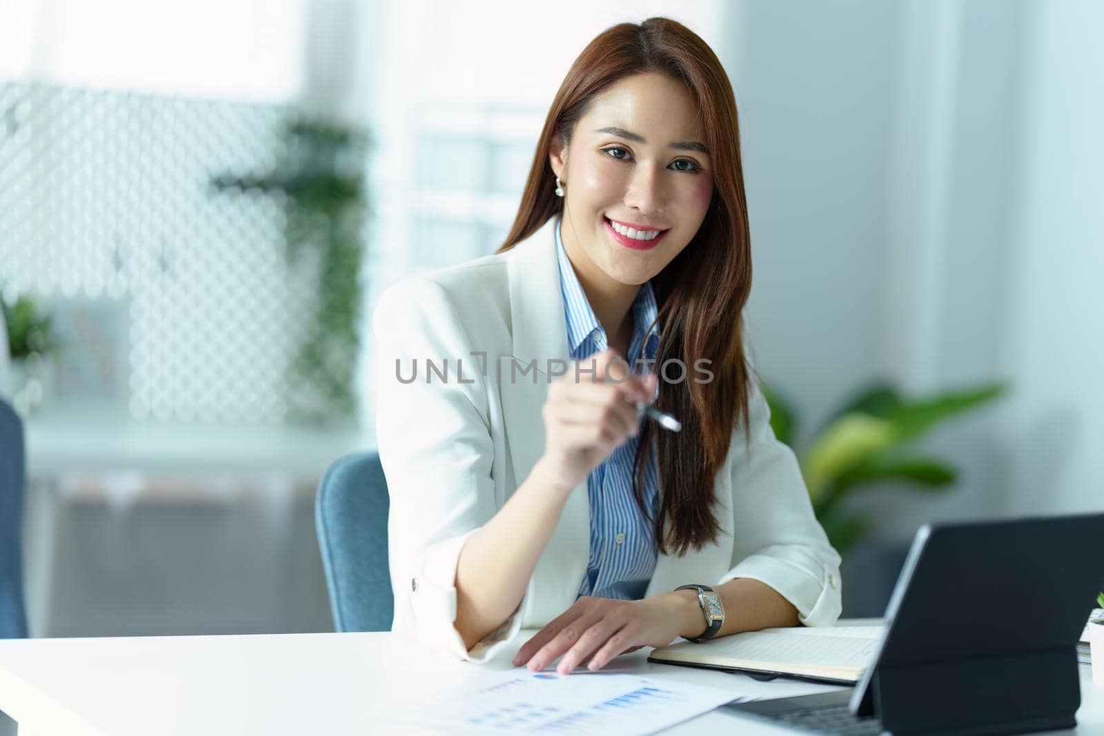 Portrait of an Asian business woman sitting at work and using a tablet computer in the office.